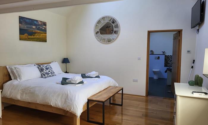 Barn room ready for guests: Super king bed with towels folded at the foot. Wooden floor, solid chunky wooden bed, with a picture of the local countrys